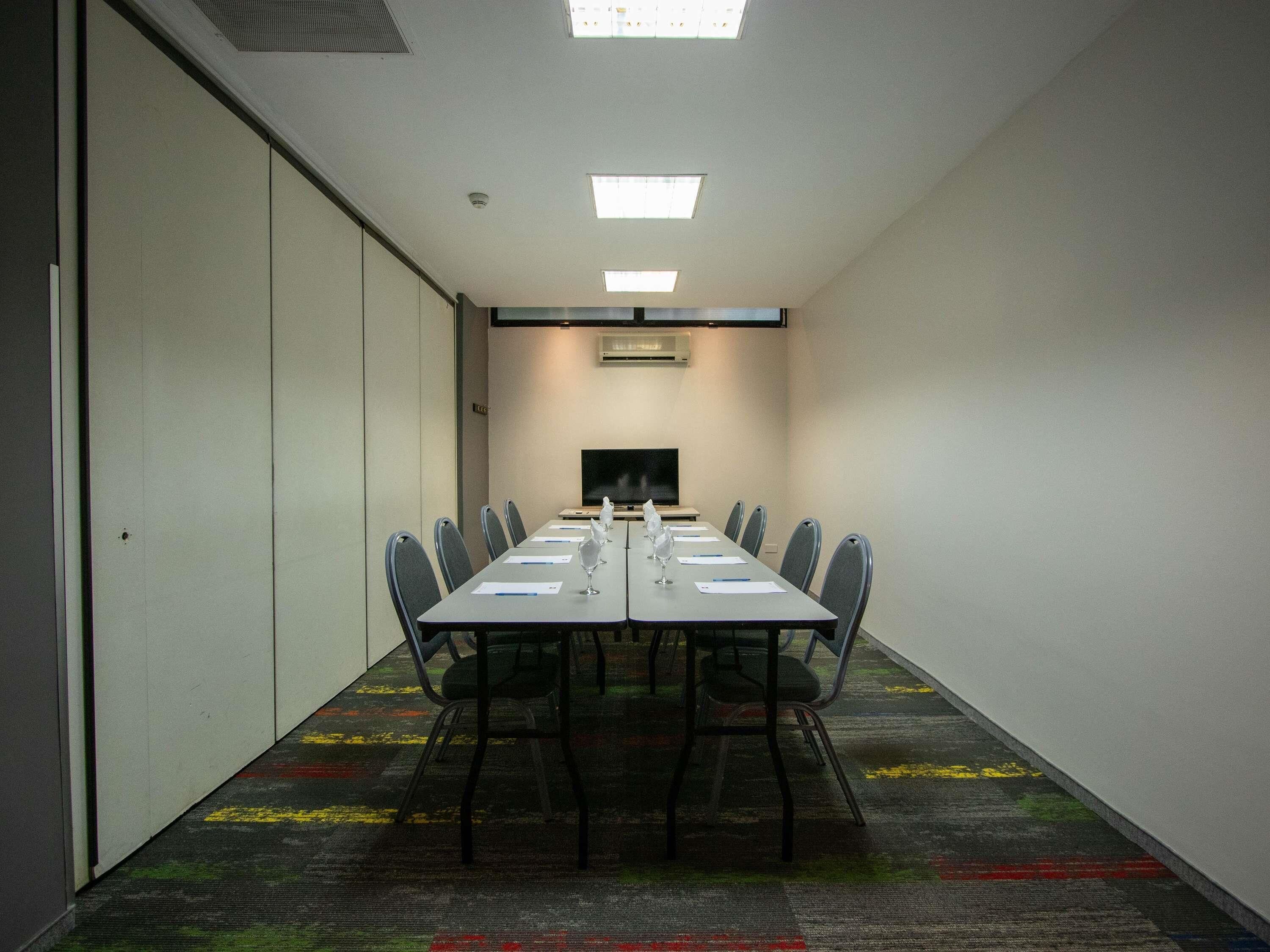 A conference room with a long table, chairs, a flat-screen TV, and a carpeted floor.