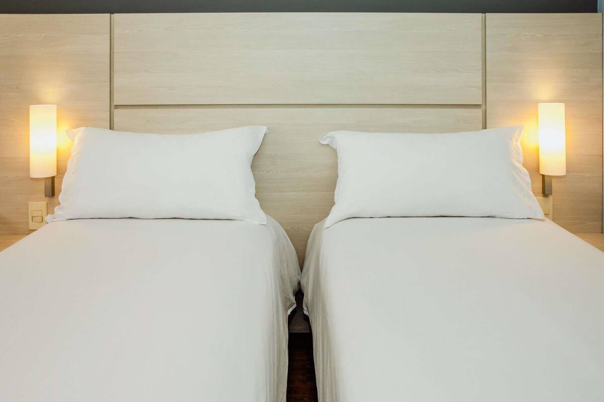 A double bed with white linens and two bedside lamps.