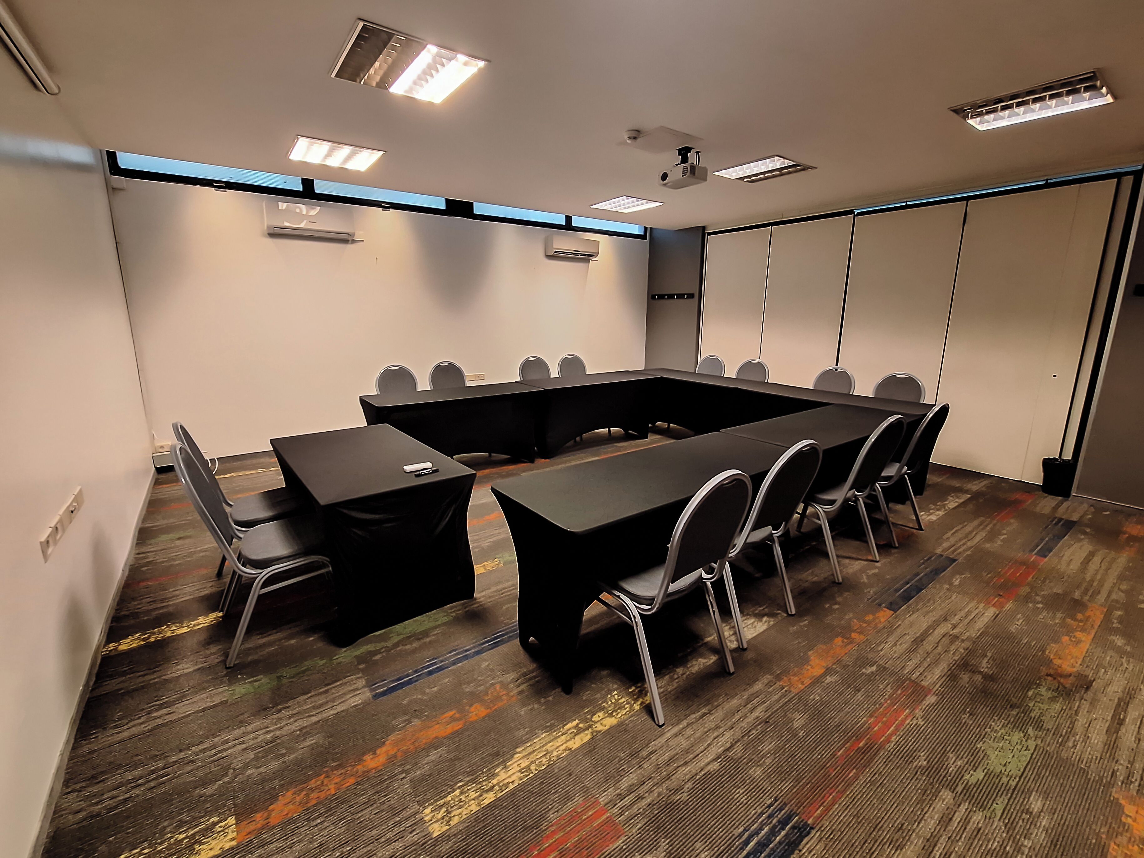 Un salón de conferencias con una larga mesa, sillas e iluminación en el techo.