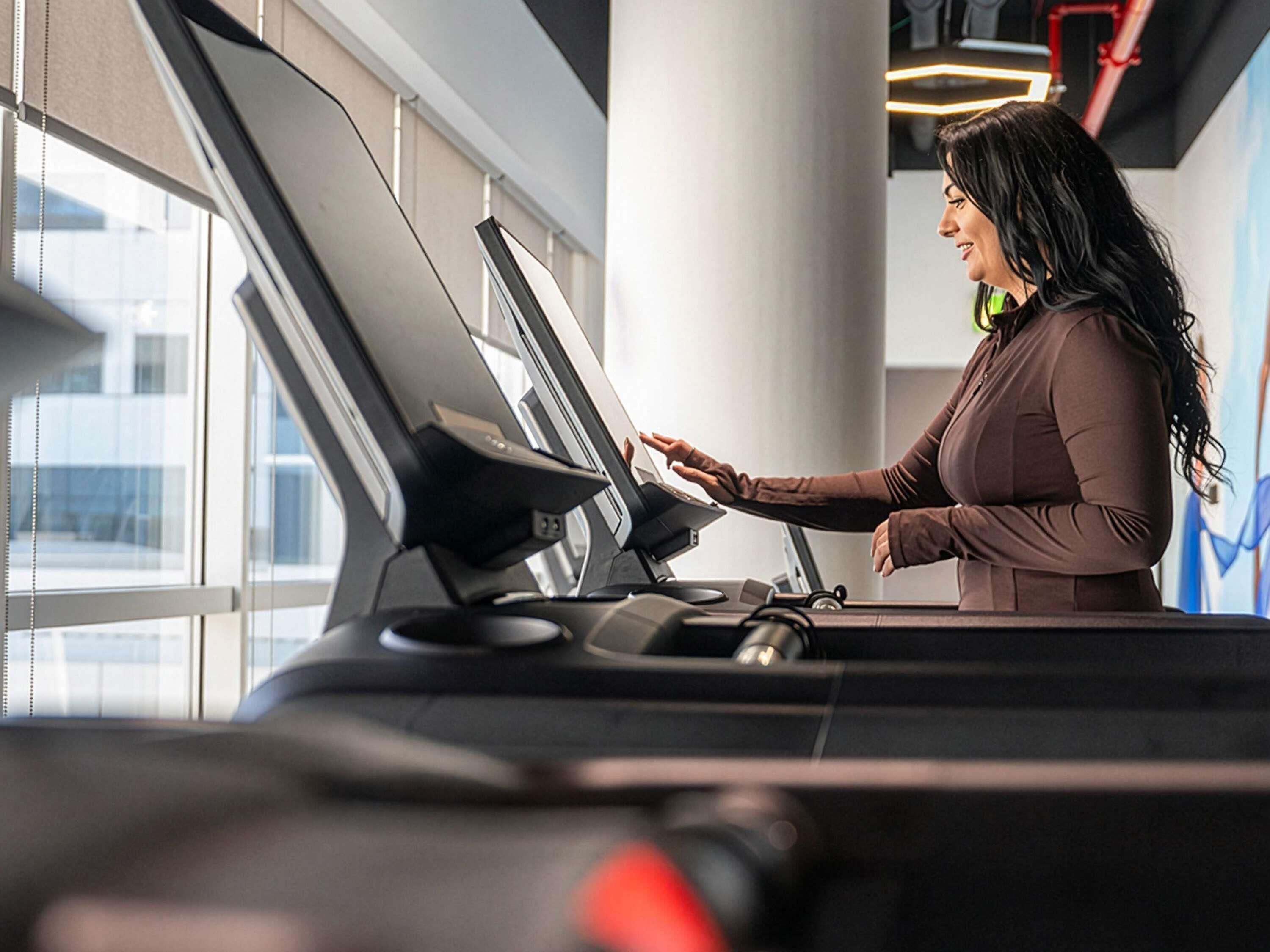 A person using a treadmill in a room with large windows and a visible cityscape.