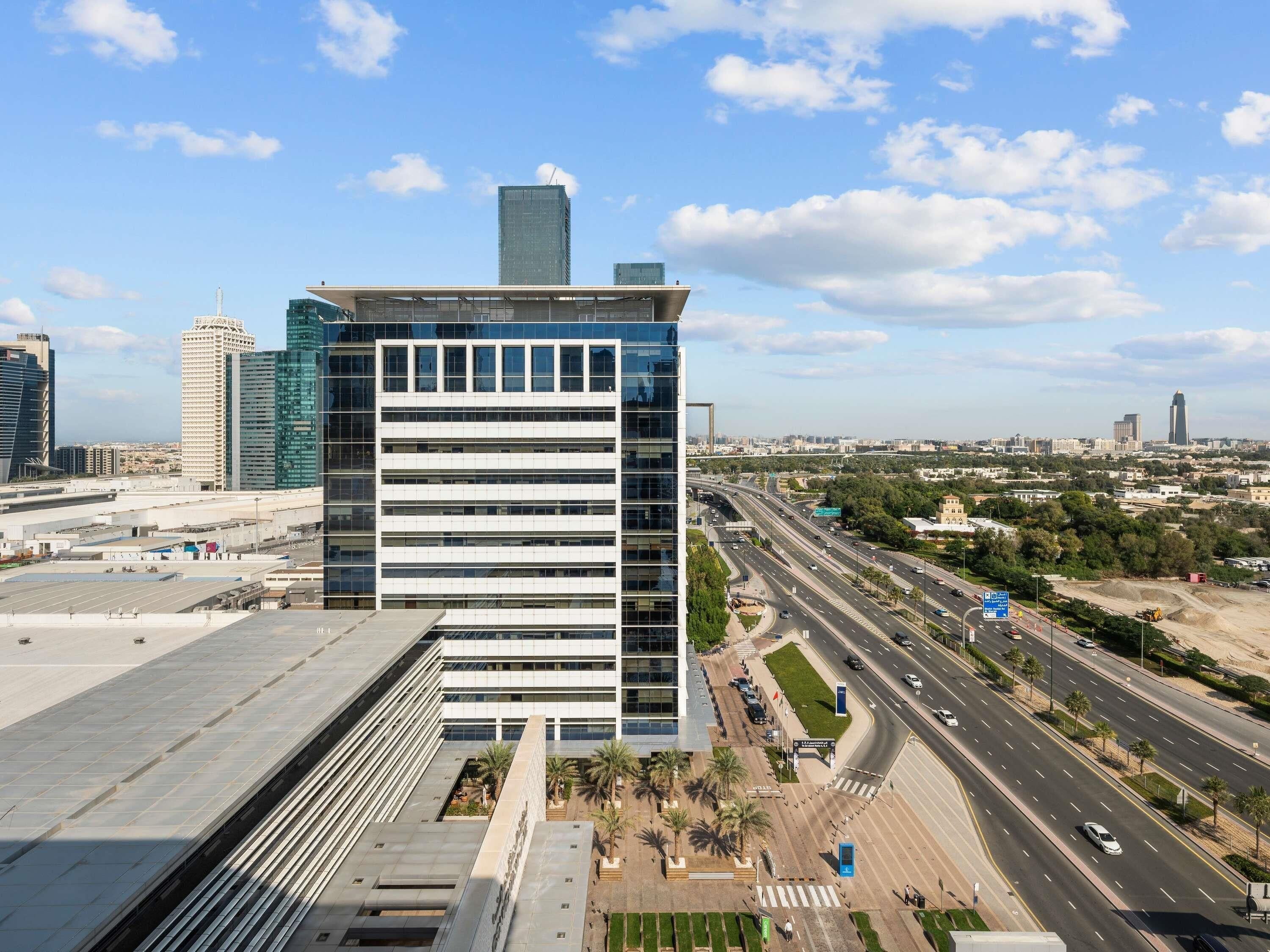 A modern building with a flat roof, large windows, and a clear view of a busy highway and cityscape in the background.