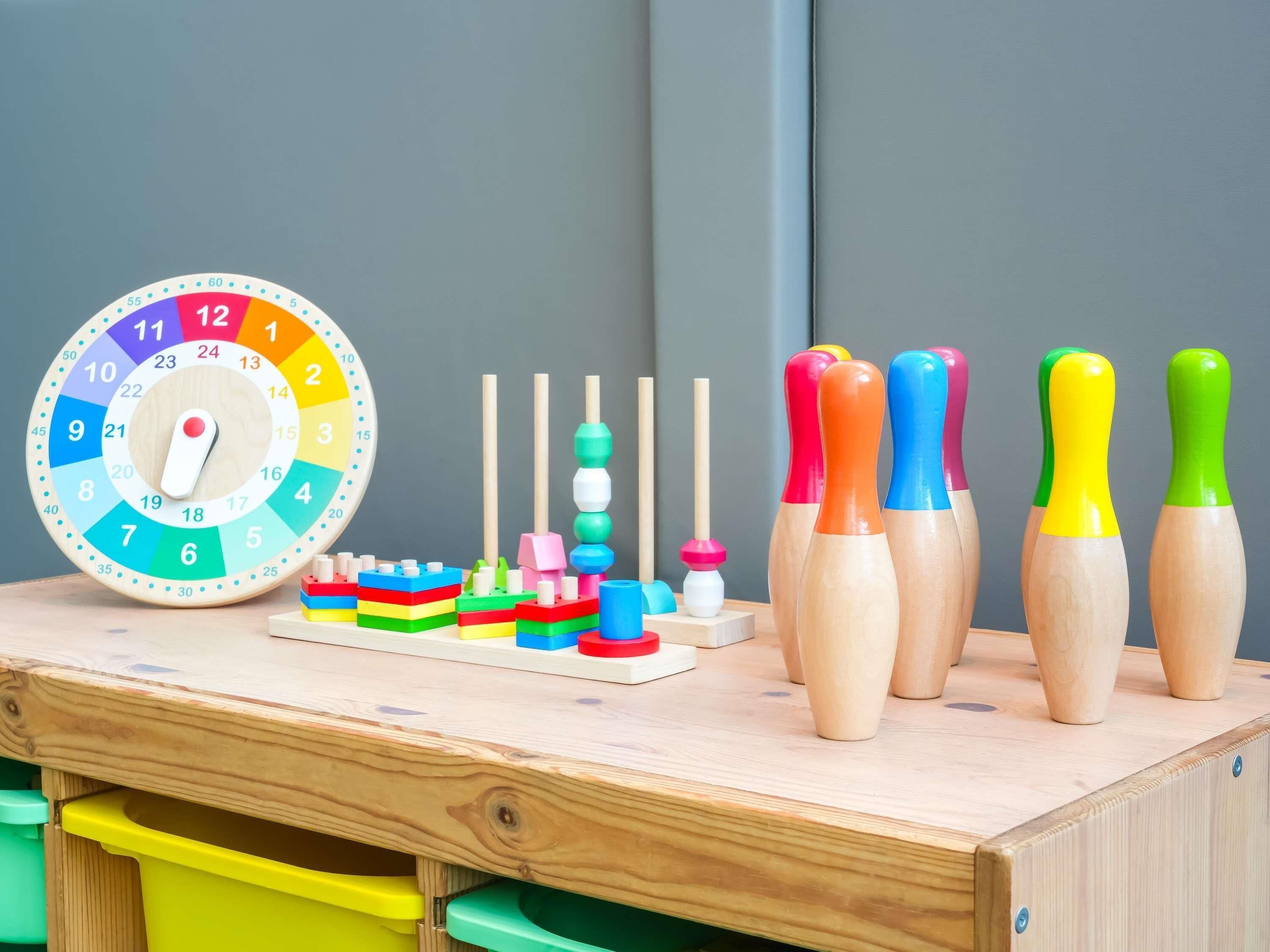 Une table en bois, une horloge colorée, un jeu de quilles en bois et un jouet composé de blocs de couleurs vives.