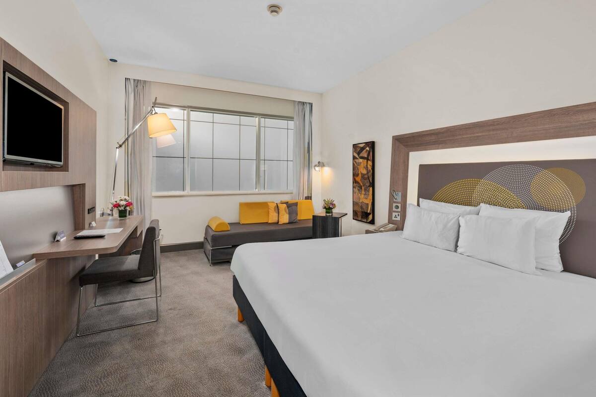 A hotel room with a bed, desk, chair, and a large window.