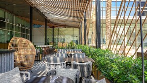 An outdoor seating area with wicker furniture, a glass enclosure, and greenery. - Novotel World Trade Centre (Dubai)