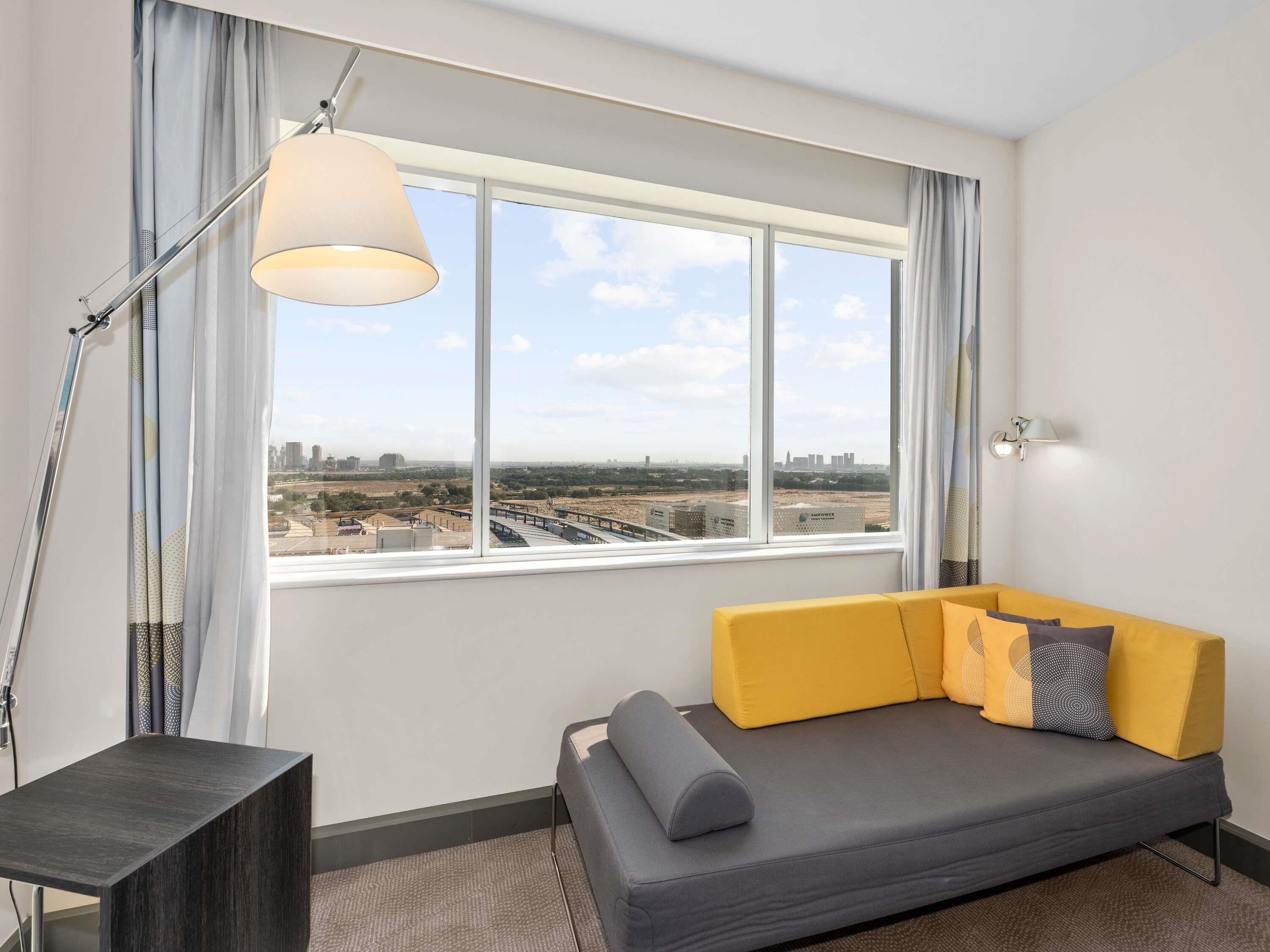 A modern room with a sofa, a lamp, a view of a cityscape, and a window with curtains.