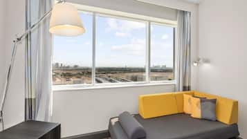 A modern room with a sofa, a lamp, a view of a cityscape, and a window with curtains.