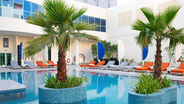An indoor swimming pool with lounge chairs and palm trees. - Novotel World Trade Centre (Dubai)