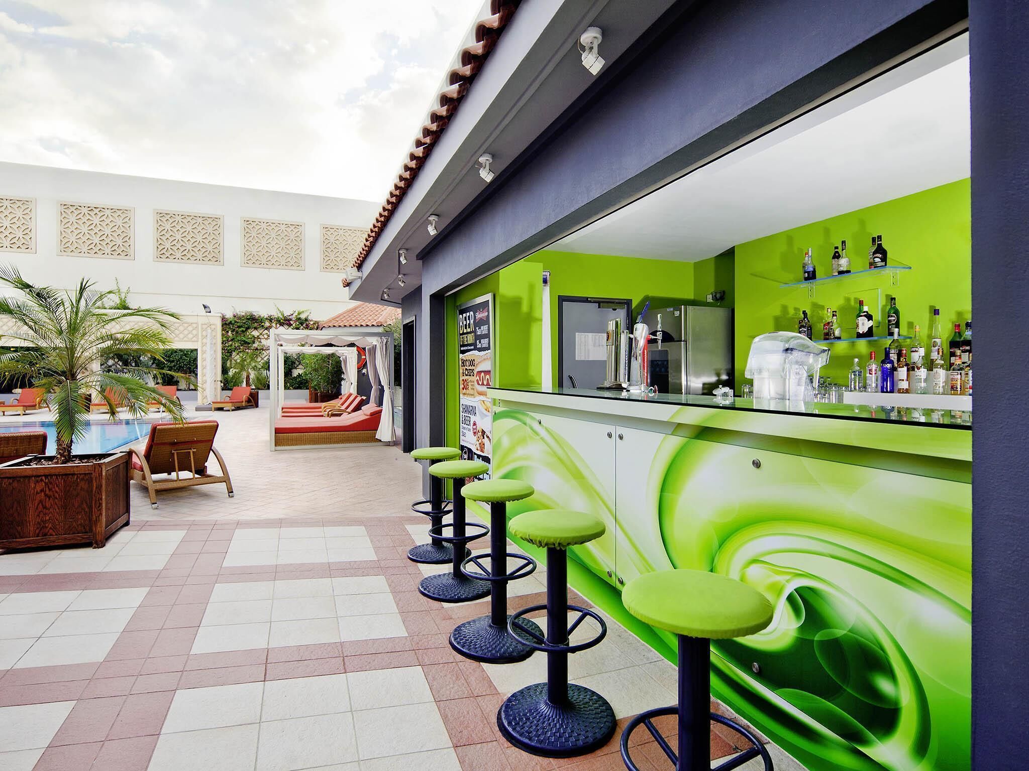 Un espace bar avec des tabourets verts, une table de billard et un coin salon abrité.