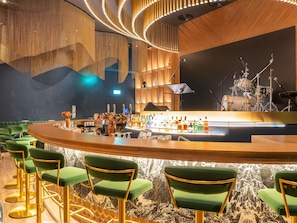 Un espace bar avec un comptoir incurvé, des tabourets de bar verts et une batterie installée au fond de la pièce.