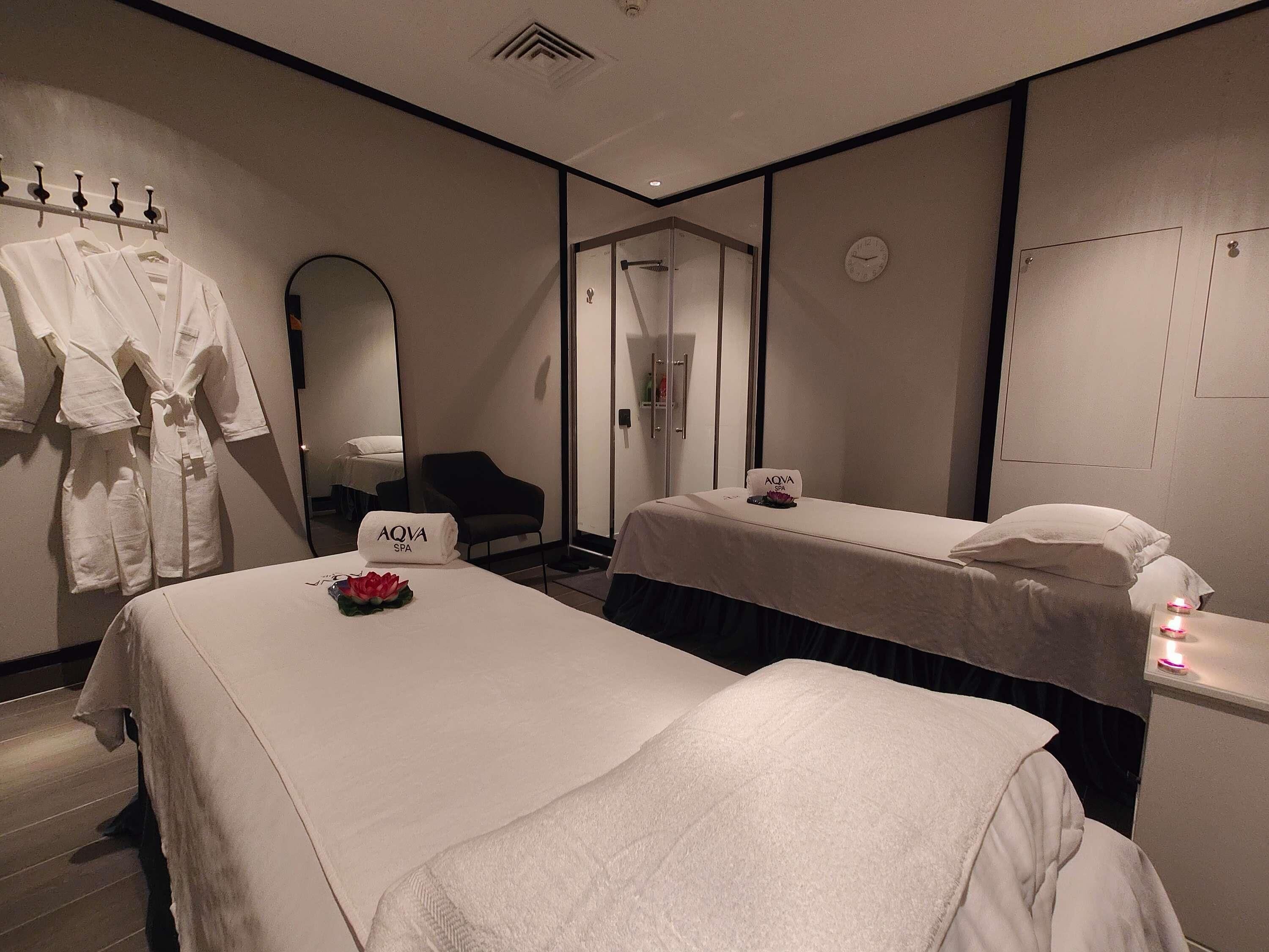 Habitación de hotel con dos camas, un perchero para bata, un espejo, un reloj y un cartel de spa.