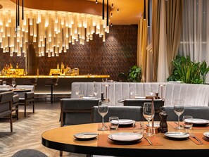 A restaurant with a bar area, round tables, and a patterned wall.