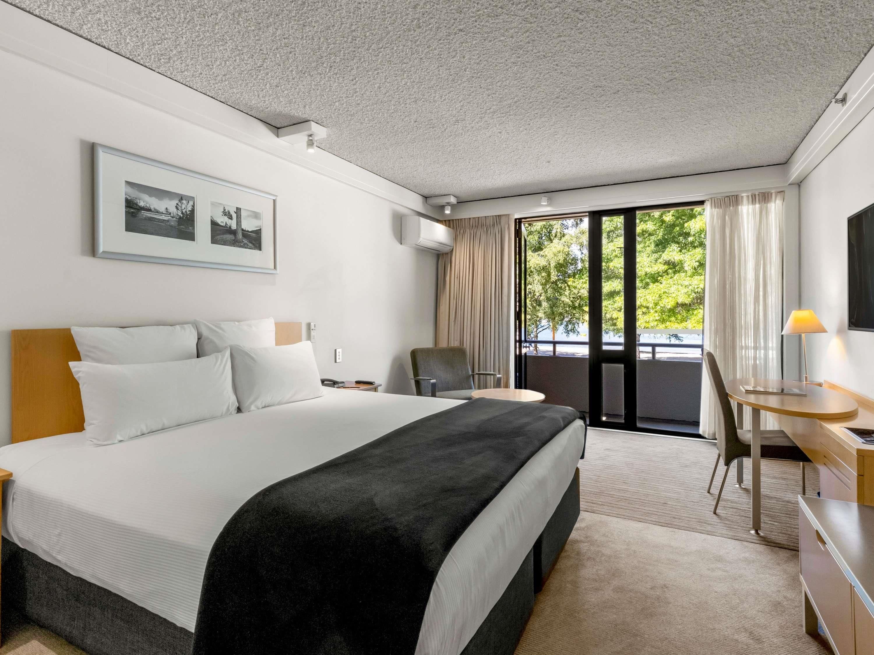 Ein Hotelzimmer mit einem großen Bett, einem Schreibtisch, einem Sessel und Blick ins Grüne.