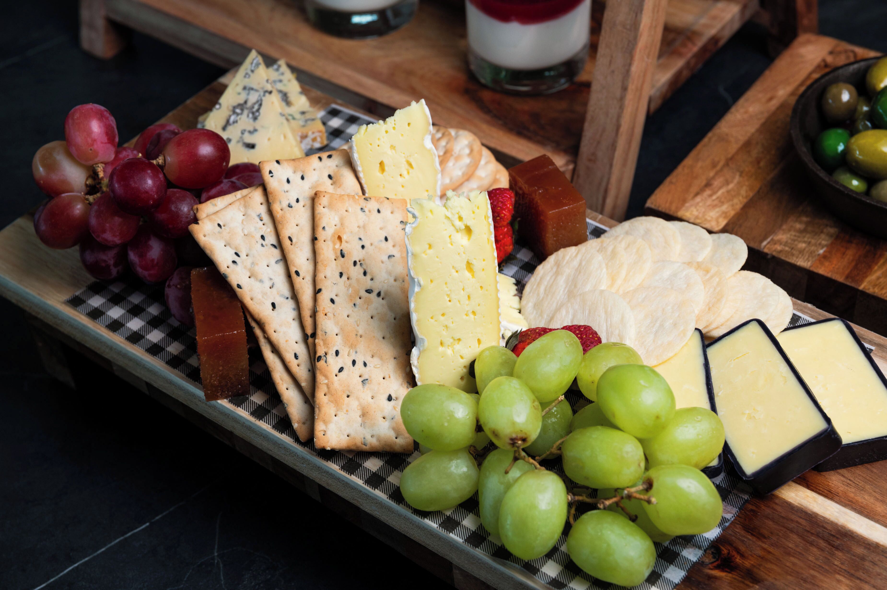 Una tabla de embutidos con diversos quesos, galletas, uvas y una fresa.