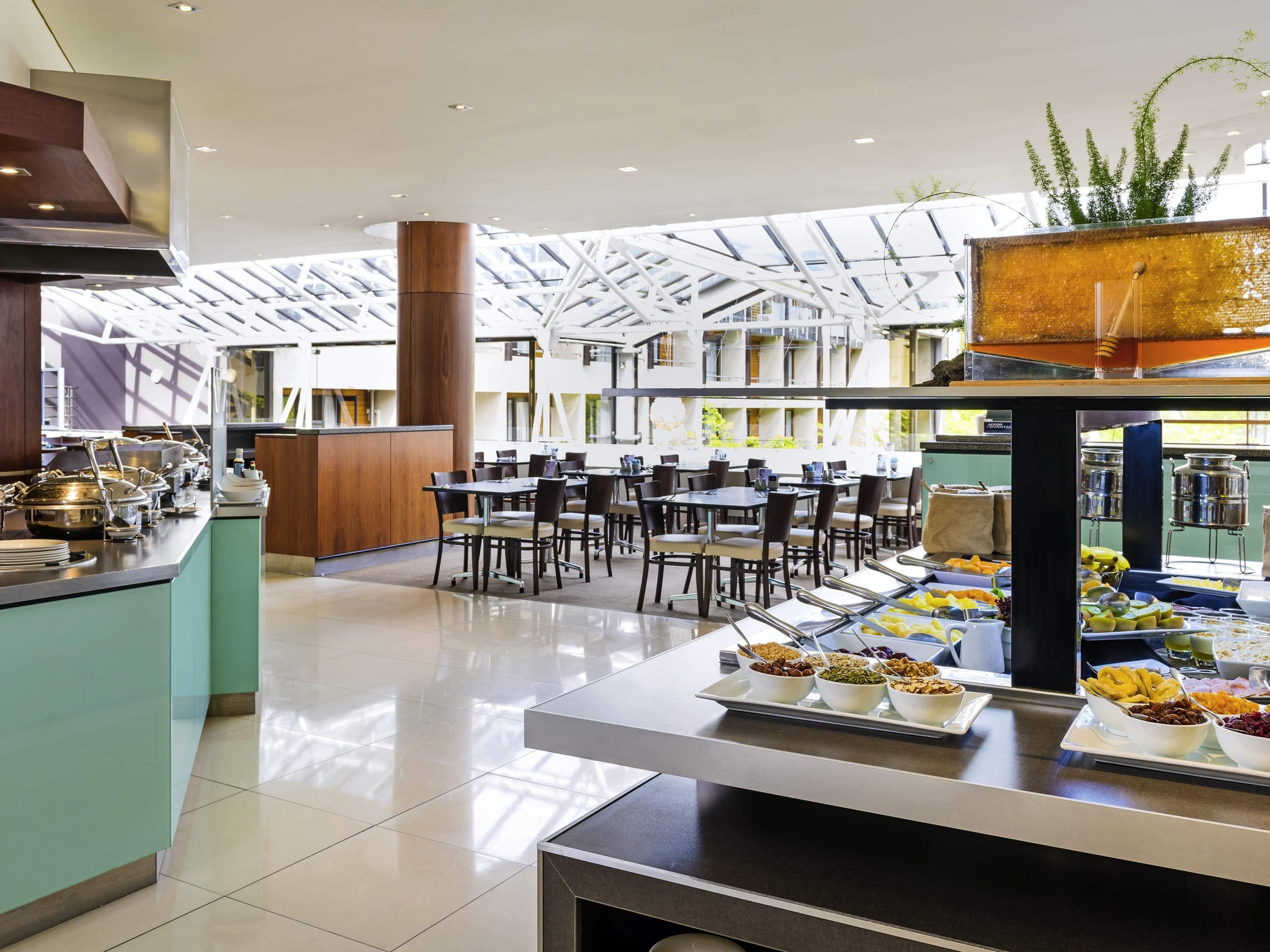 A modern dining area with a high ceiling, glass panels, and a buffet with various food items.
