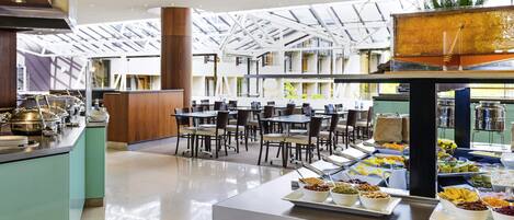 A modern dining area with a high ceiling, glass panels, and a buffet with various food items.