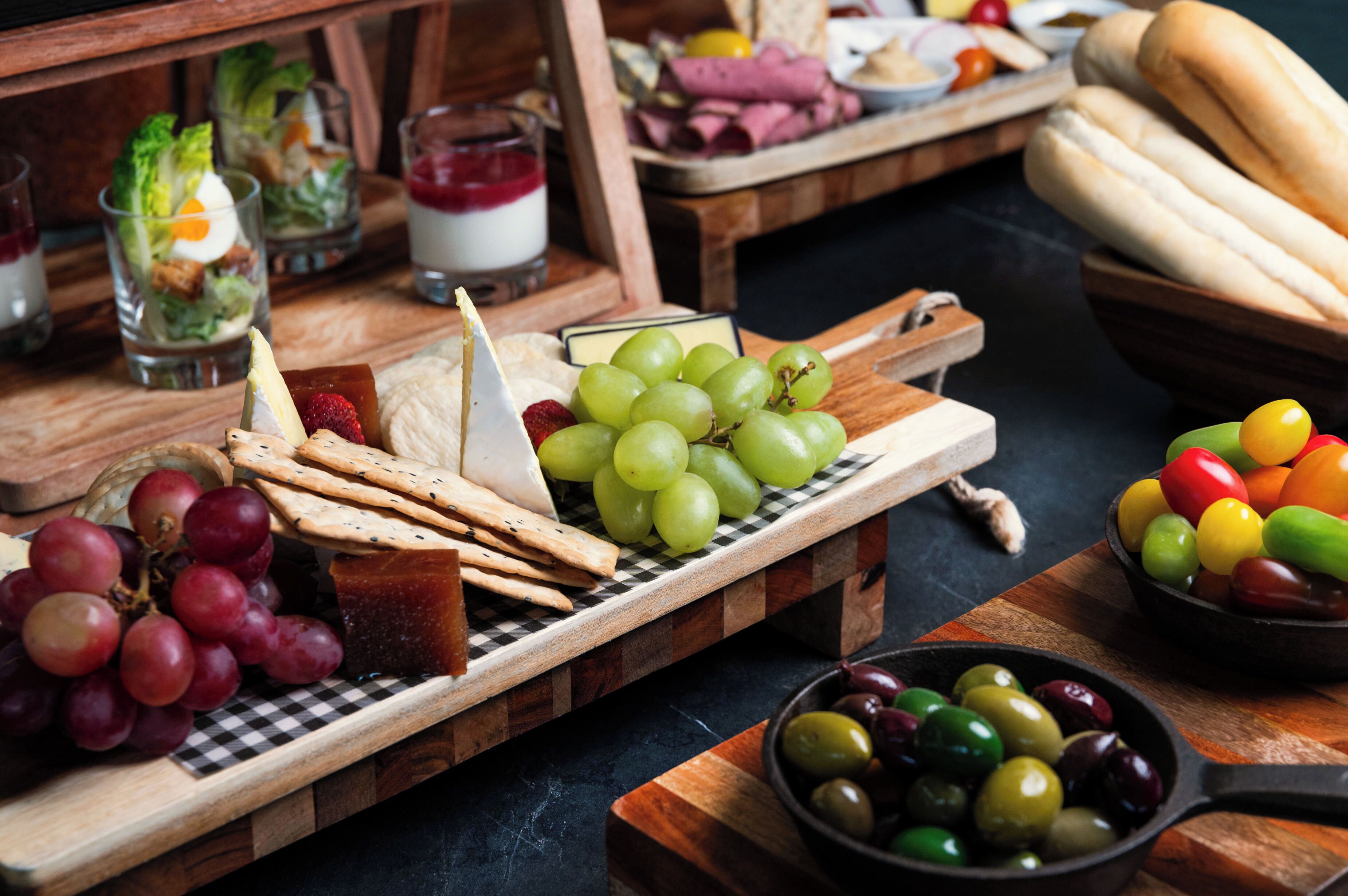 A wooden board with various cheeses, grapes, and crackers.