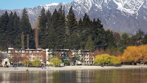 A lakeside view with a mountain backdrop, a row of buildings, and a park with trees. - Novotel Queenstown Lakeside (Queenstown)