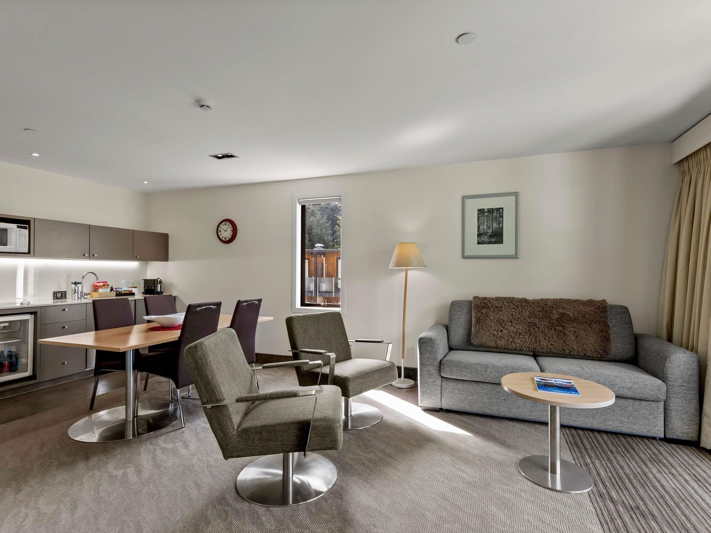 Quarto de hotel moderno com área de jantar, sofá, luminária e quadro na parede.