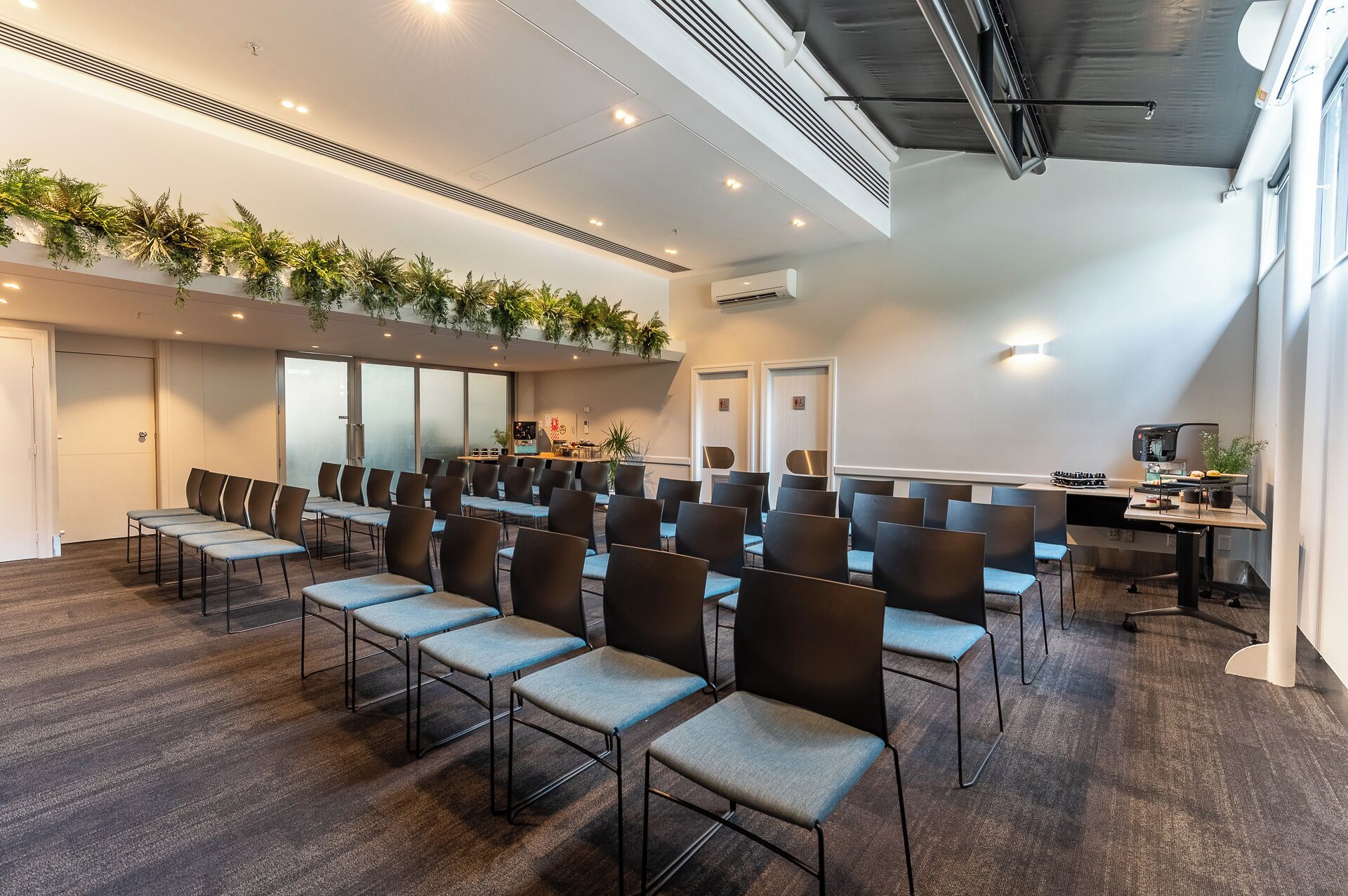 Une salle de conférence avec des rangées de chaises, un coin cuisine et une grande fenêtre.
