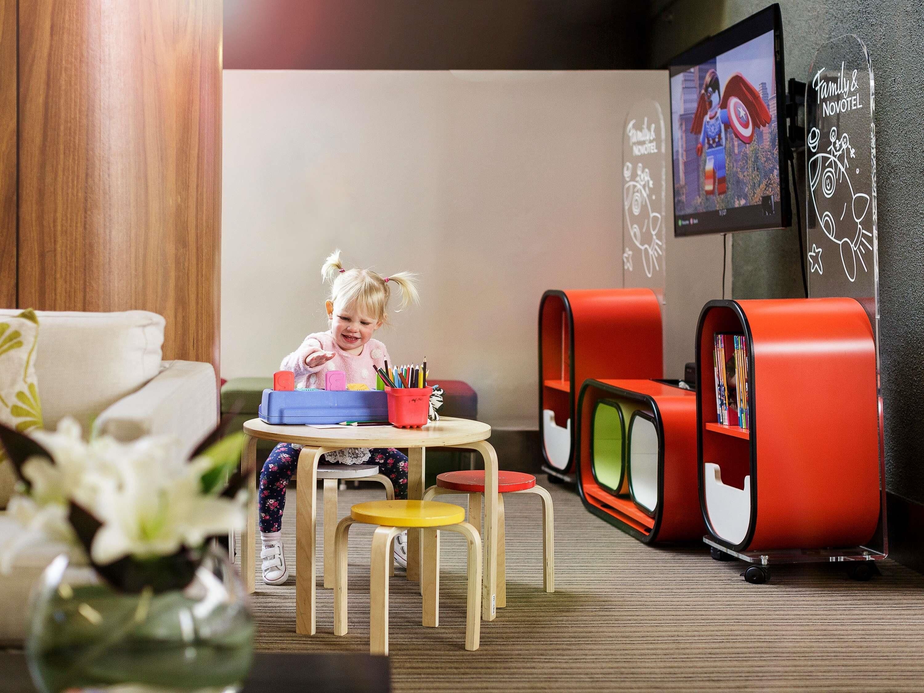 A child at a table with toys and a TV in the background.