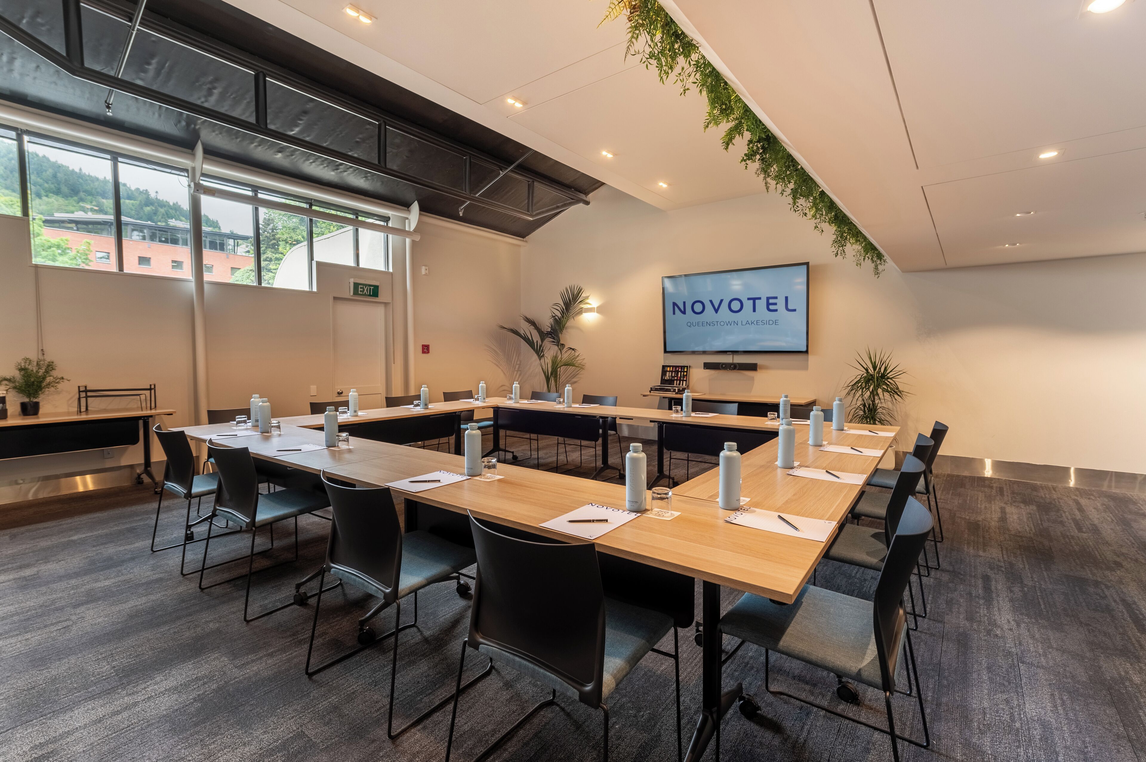 A conference room with long tables, chairs, and a TV screen displaying 'NOVOTEL'.