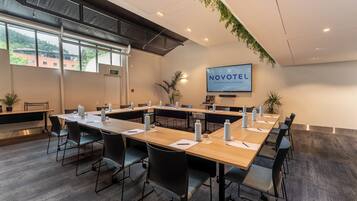 A conference room with long tables, chairs, and a TV screen displaying 'NOVOTEL'.