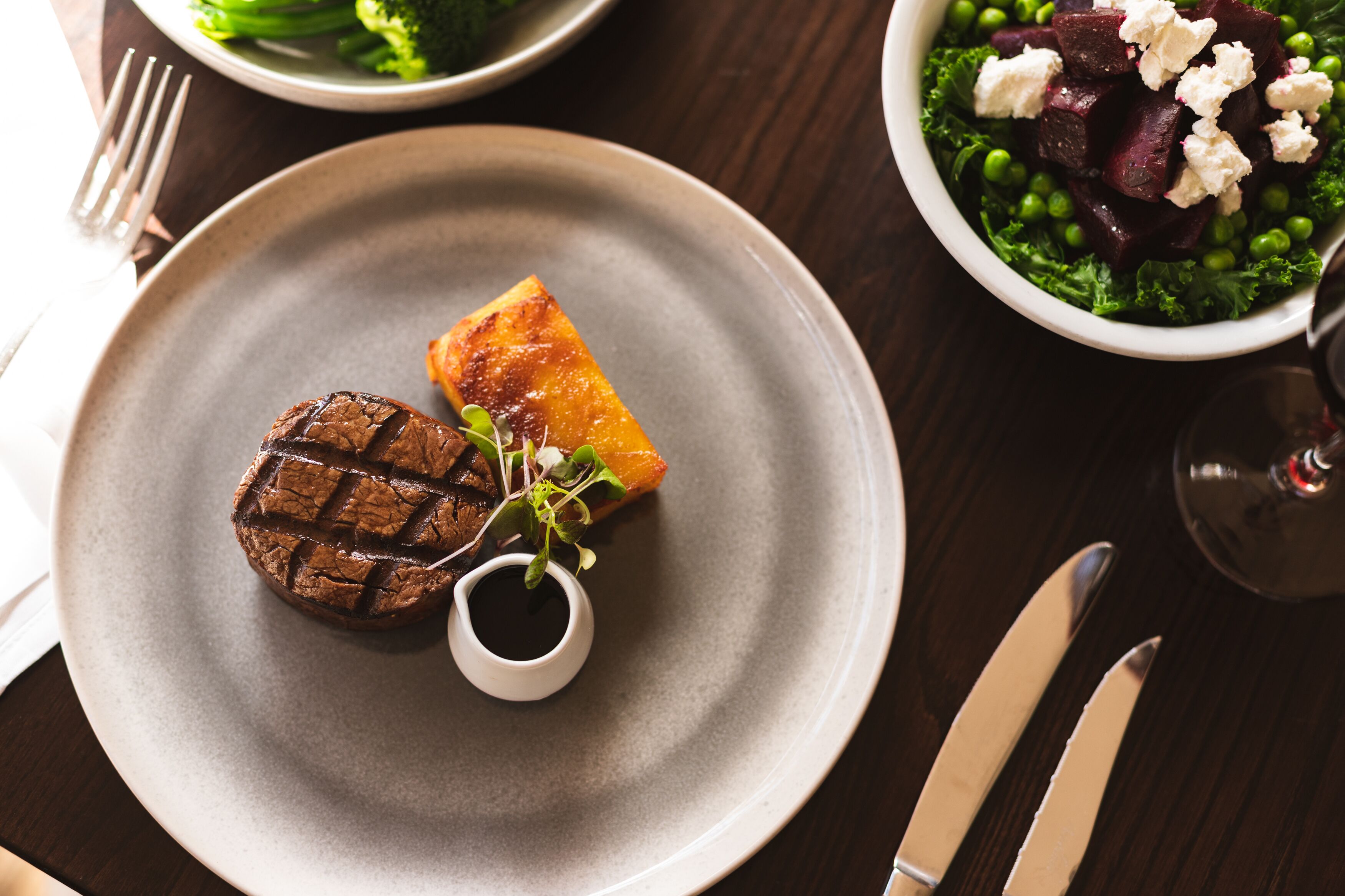 A plate with a grilled steak and a piece of grilled fruit, accompanied by a small cup of sauce.