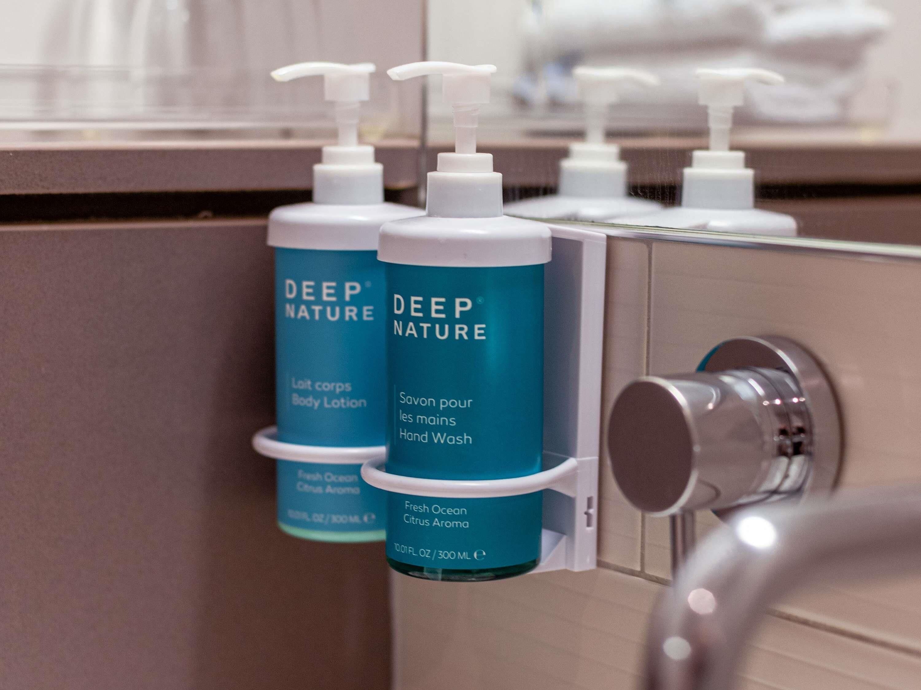 Ein Badezimmer mit einem Seifenspenderhalter, der zwei Flaschen Deep Nature Body Lotion und Handseife enthält.