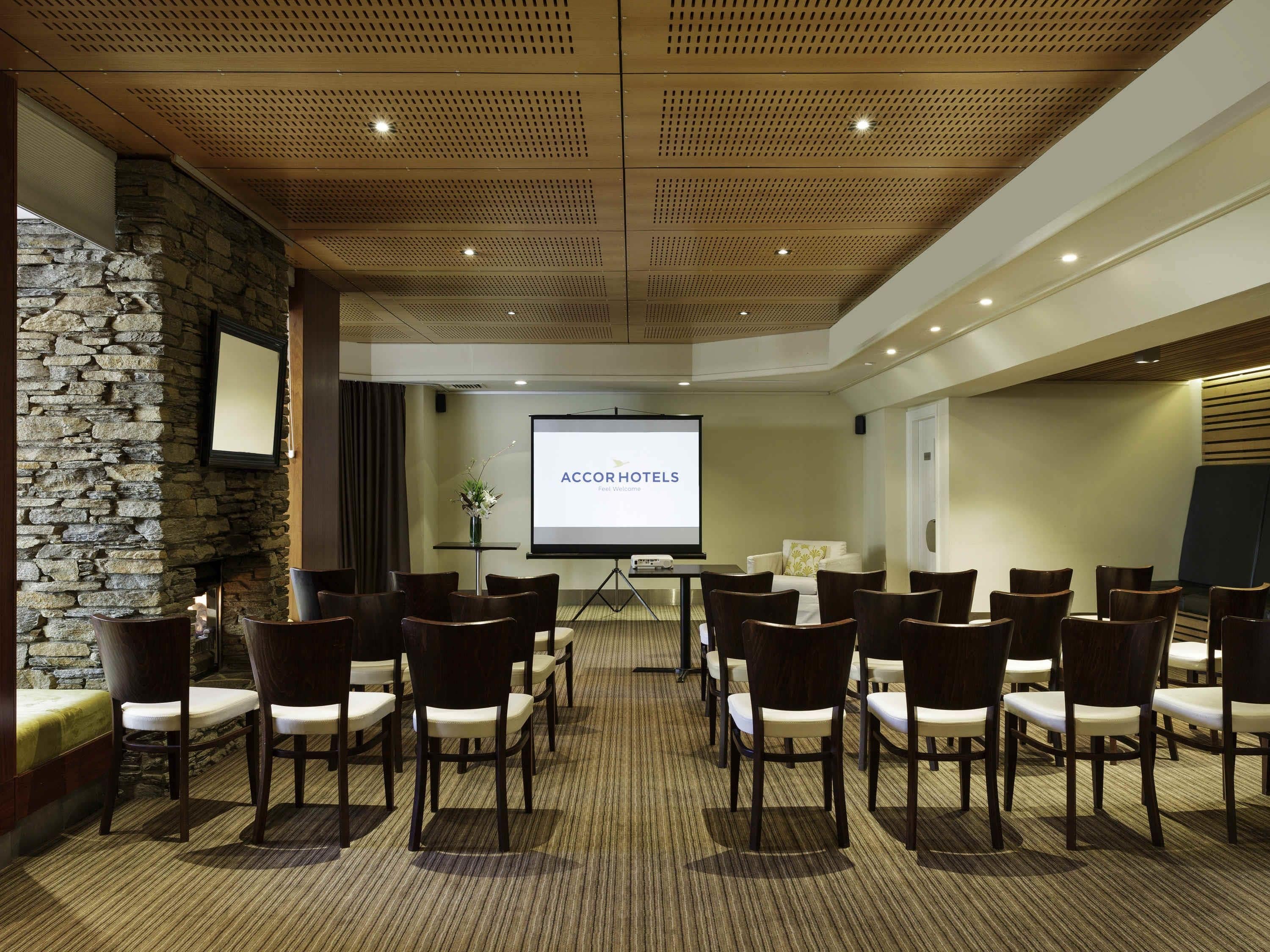 Una sala de conferencias con pared de piedra, una pantalla de proyección y varias sillas dispuestas para una reunión.