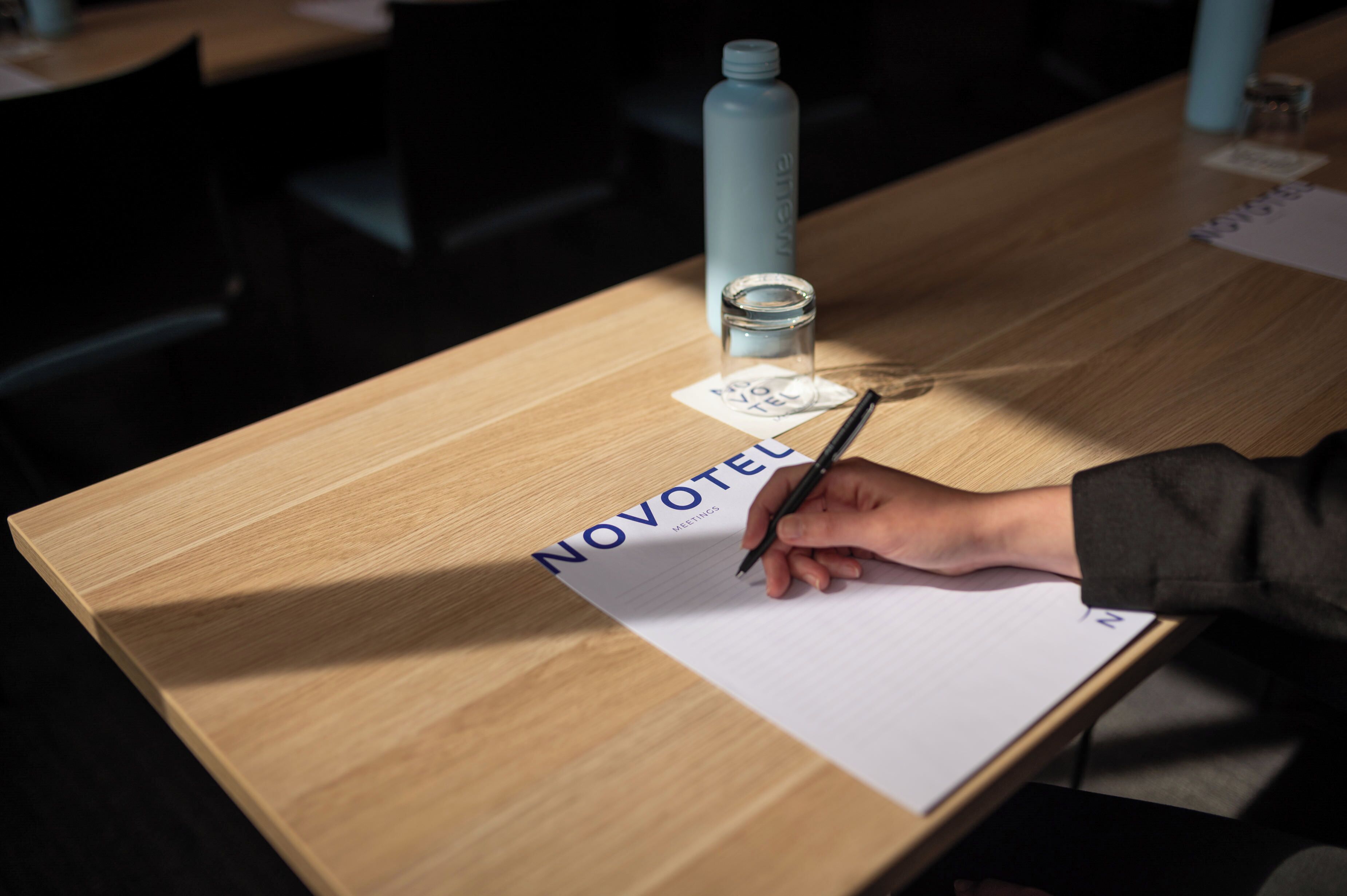 Une table en bois, sur laquelle se trouvent un bloc-notes portant l’inscription « NOVOTEL » et un stylo.