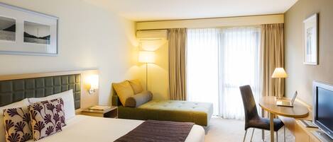 A hotel room with a bed, a desk with a laptop, a chair, a lamp, and a TV.