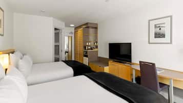 Habitación de hotel con dos camas, un escritorio con televisor, una silla y una kitchenette.