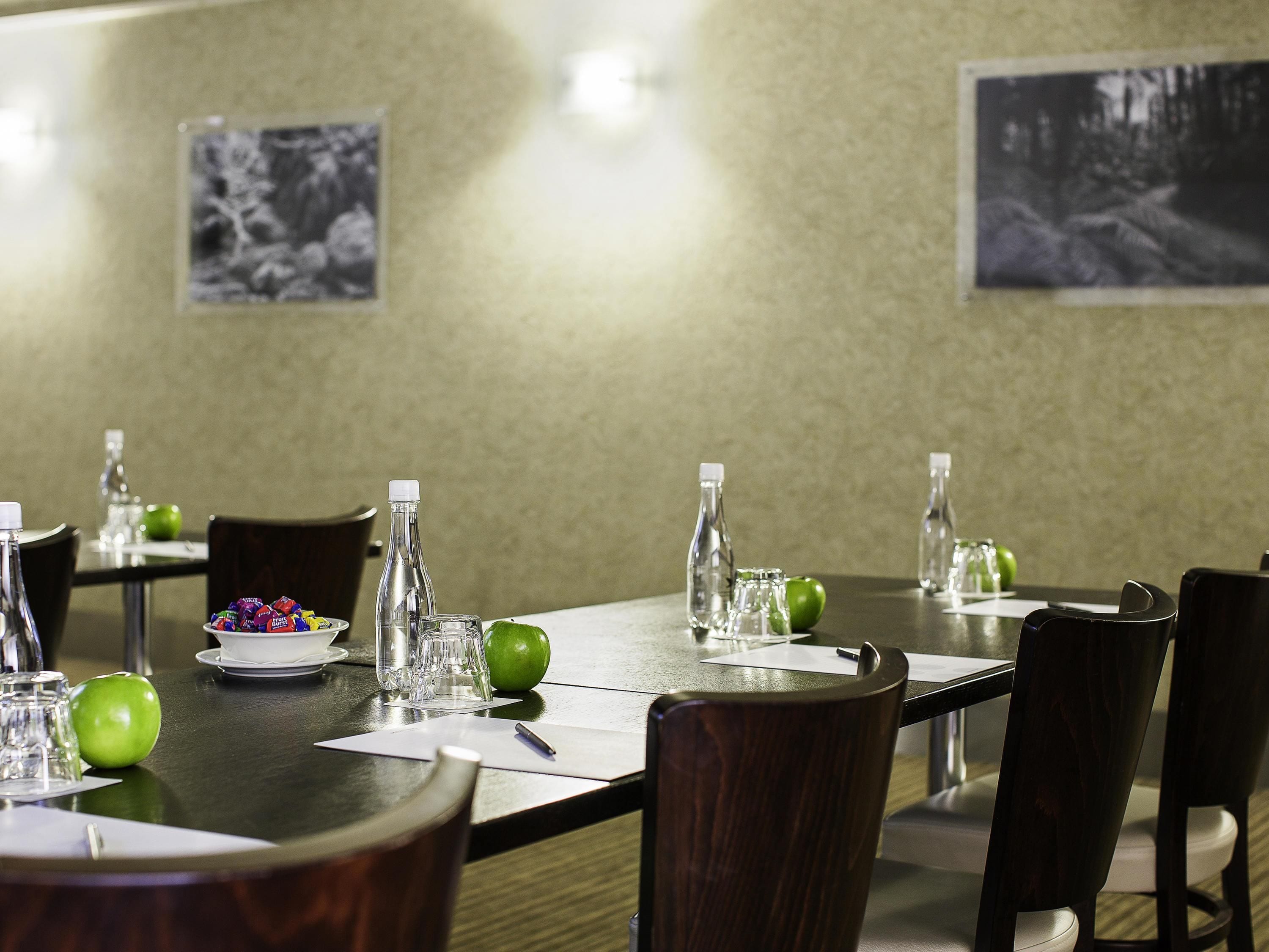 A conference room with a long table, chairs, water bottles, glasses, and apples.