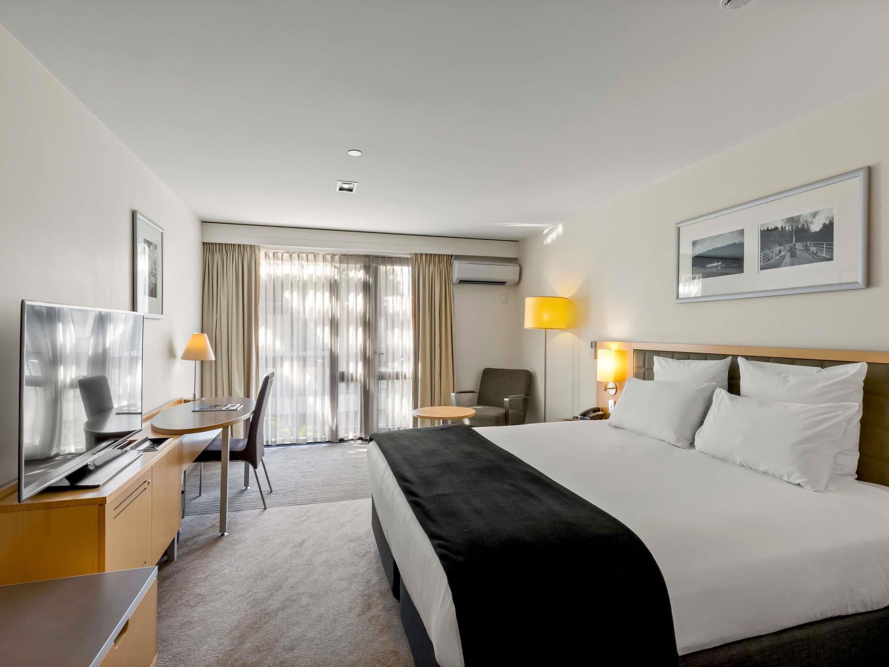 A hotel room with a bed, a desk, a chair, a TV, and a window with curtains.