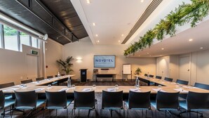 A conference room with a long table, black chairs, a TV screen, and a sign reading "NOVOTEL". - Novotel Queenstown Lakeside (Queenstown)