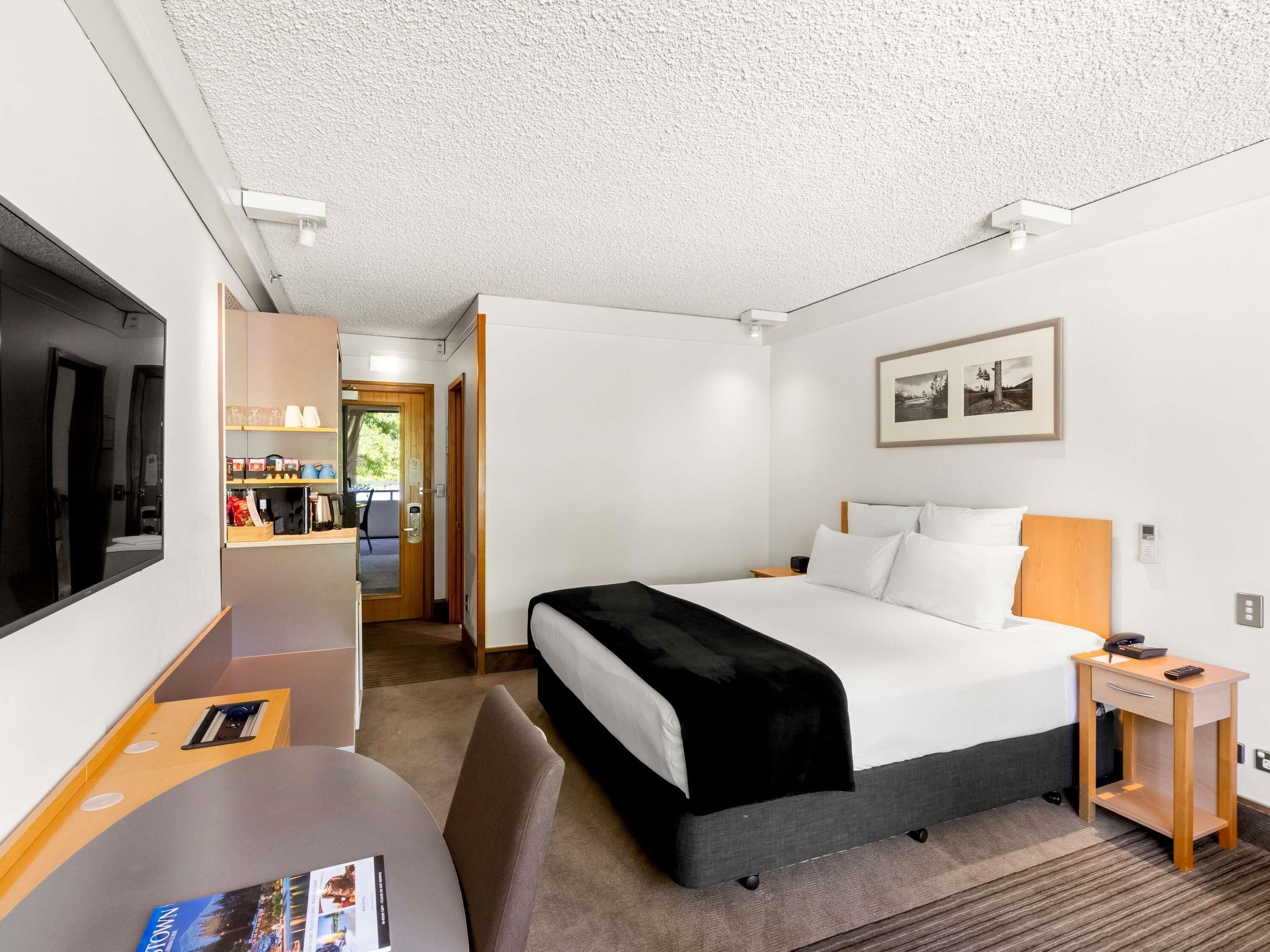 Quarto de hotel com cama, mesa de cabeceira, televisão e escrivaninha com cadeira.