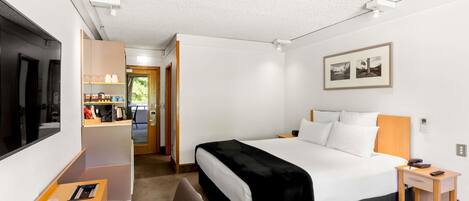 Quarto de hotel com cama, mesa de cabeceira, televisão e escrivaninha com cadeira.