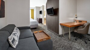 Hotelkamer met een bank, een houten bureau, een stoel, een televisie en een dienbladtafel.