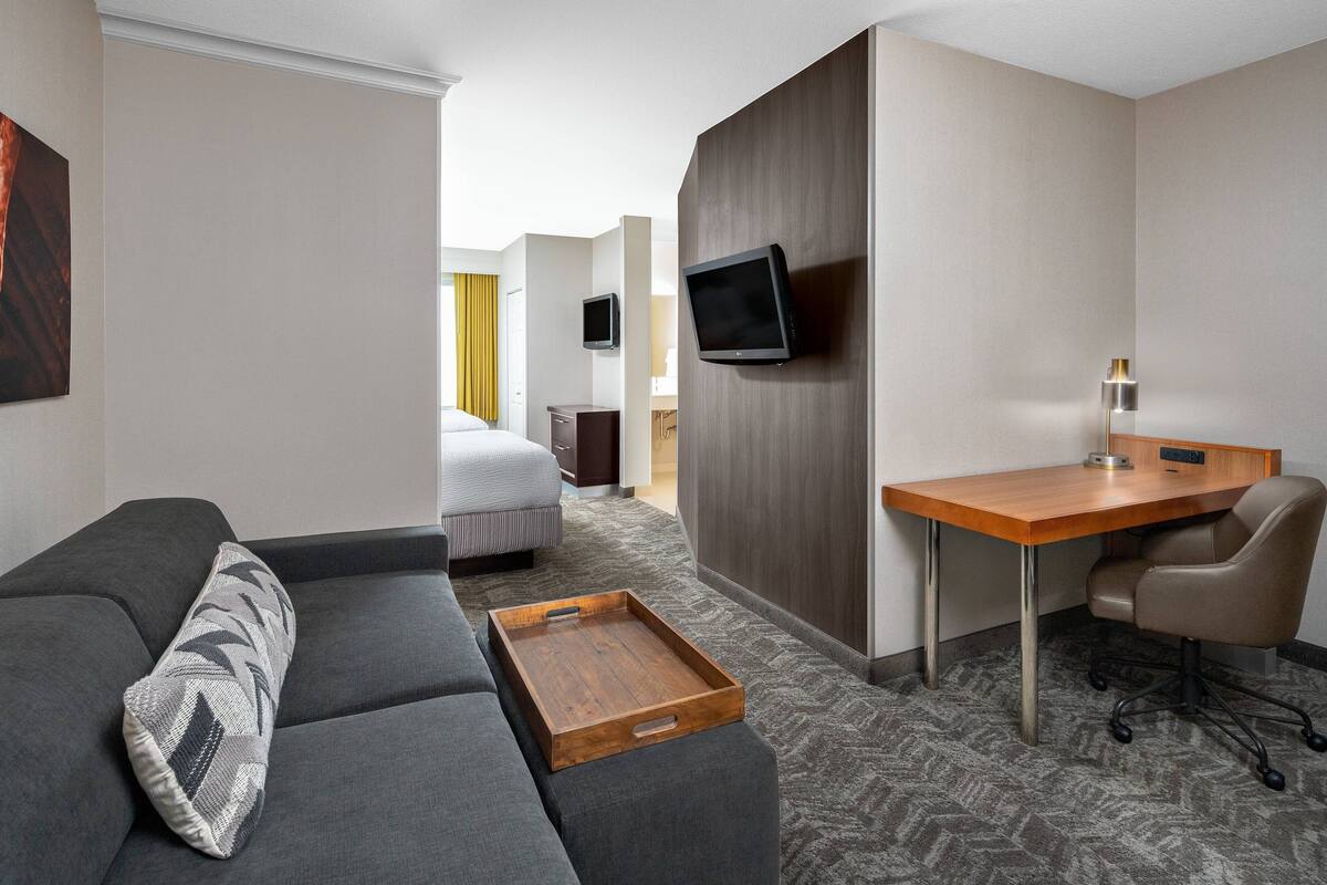 Ein Hotelzimmer mit einer Couch, einem Holztisch, einem Stuhl, einem Fernseher und einem Tablett.