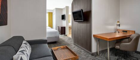 Habitación de hotel con sofá, escritorio de madera, silla, televisión y mesita.