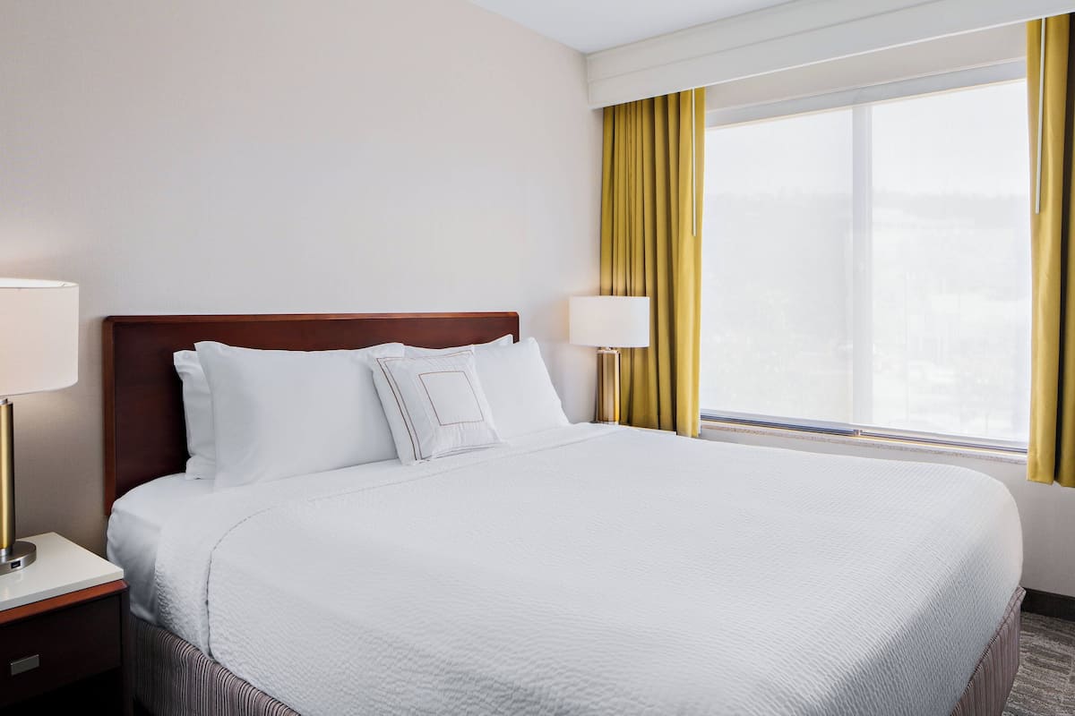 Ein Hotelzimmer mit einem großen Bett, zwei Nachttischen und einem Fenster mit Vorhängen.