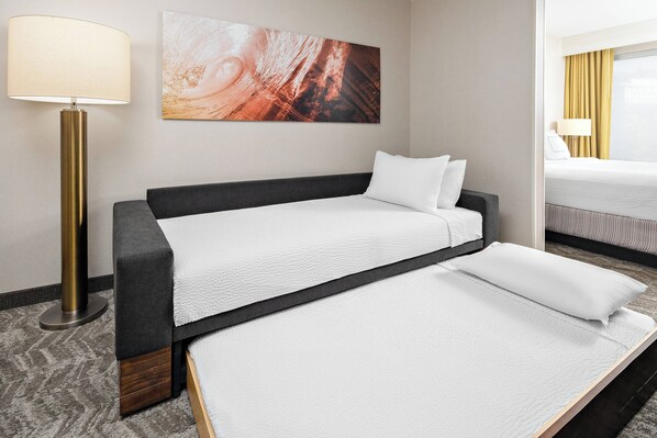 A hotel room with a single bed, a bedside table, a lamp, and a large abstract painting on the wall.