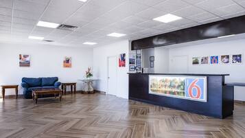 A reception area with a wooden herringbone floor, a blue sofa, a small table, and a reception desk with a '6' sign.