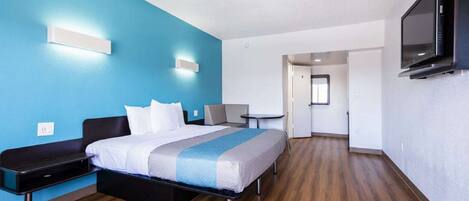 Una habitación de hotel con cama, escritorio, silla, televisor y una mesita.