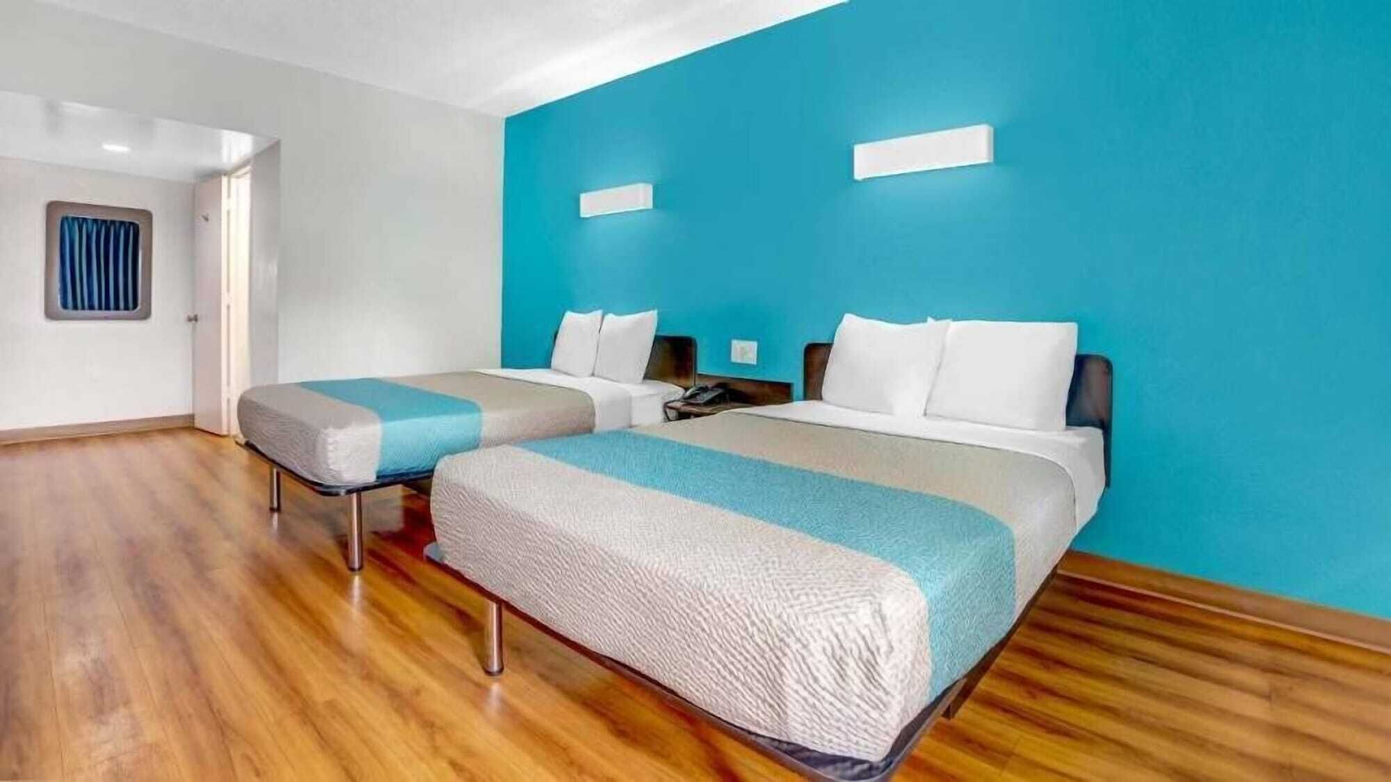 A hotel room with two beds, a wooden floor, and a blue accent wall.