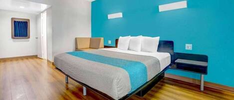 A hotel room with a bed, a nightstand, a blue accent wall, and wooden flooring.