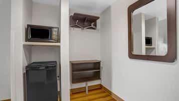 A compact bathroom with a microwave, a trash bin, a shelf with hangers, and a mirror.