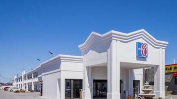Um motel com um grande letreiro '6', várias unidades e uma fonte em frente.