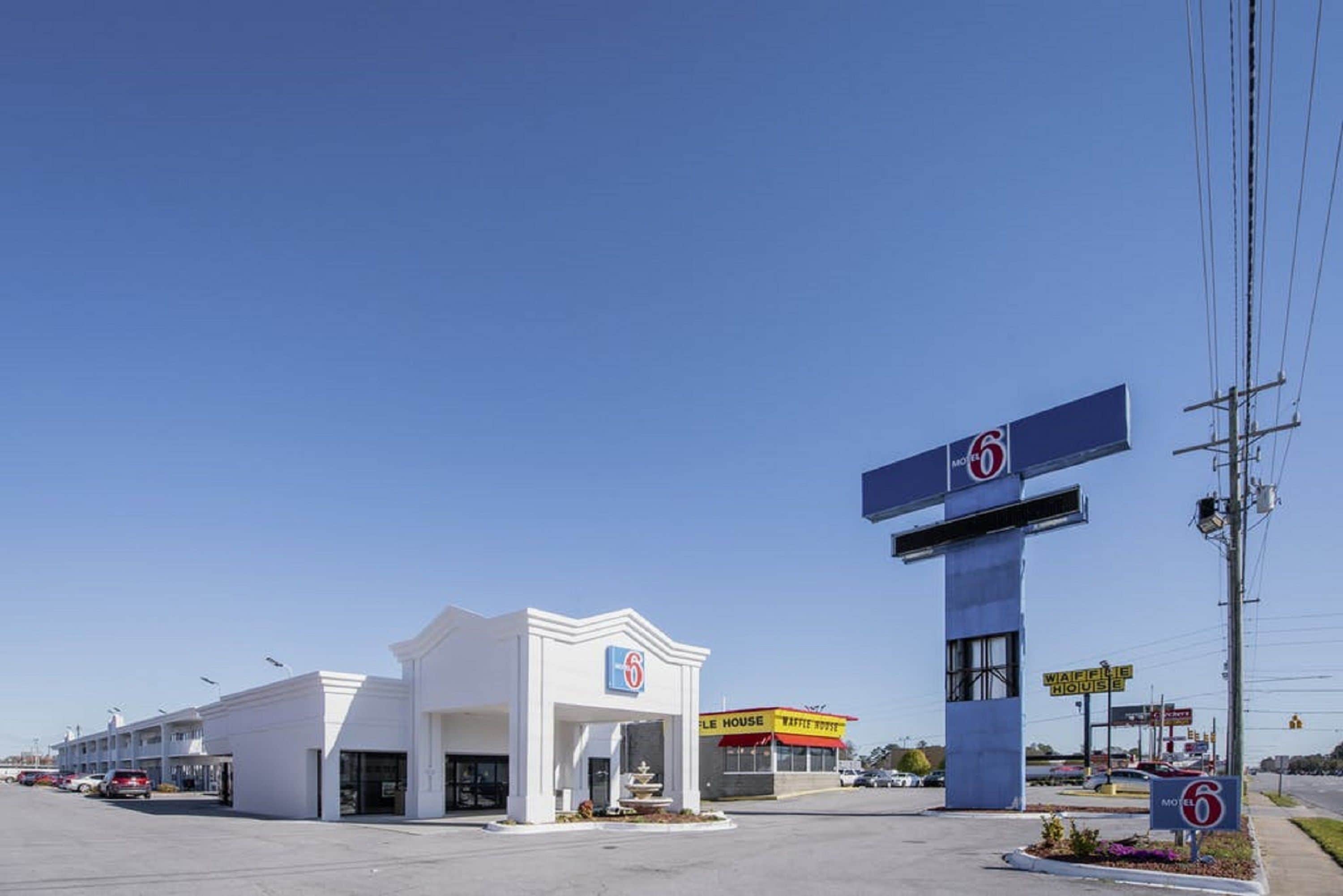 A motel with a prominent '6' sign, a 'Waffle House' across the street, and a clear blue sky.