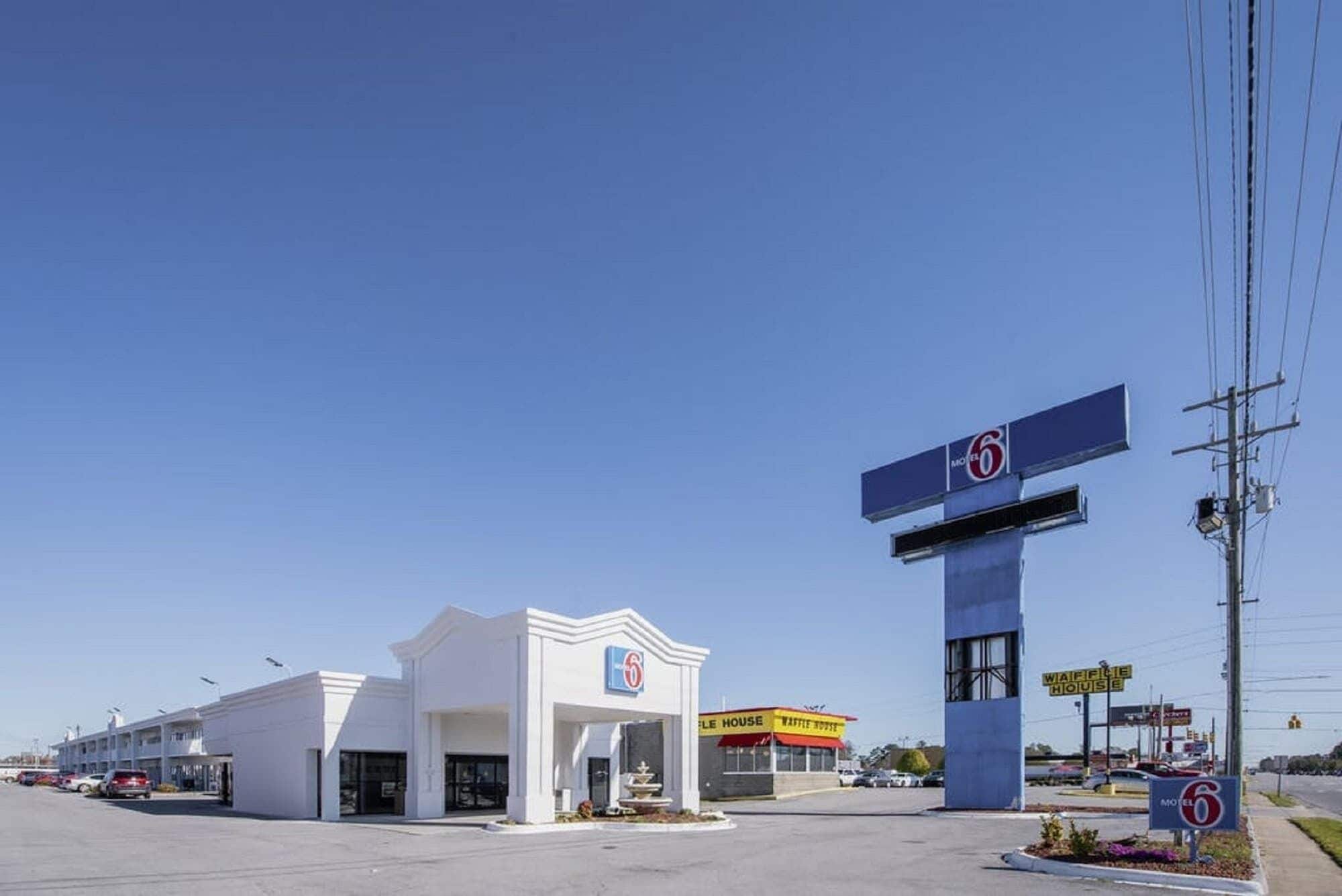 A motel with a prominent '6' sign, a drive-thru, and a visible 'Waffle House' across the street.